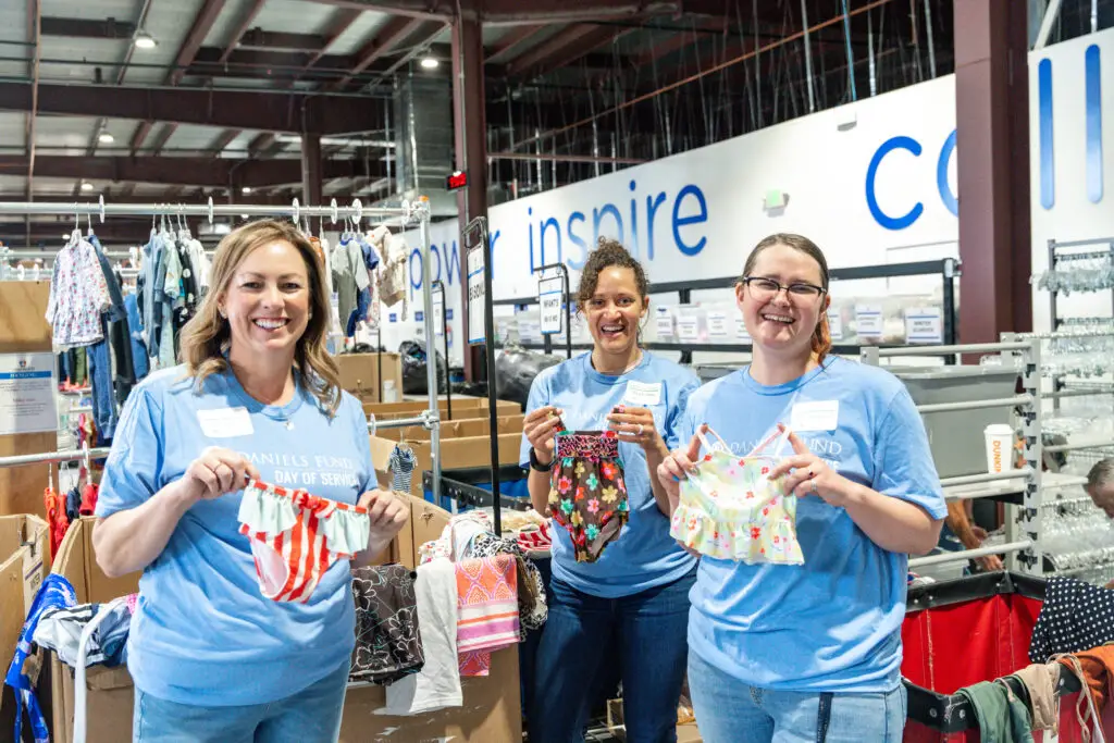 Three women smiling and organizing baby clothes together.