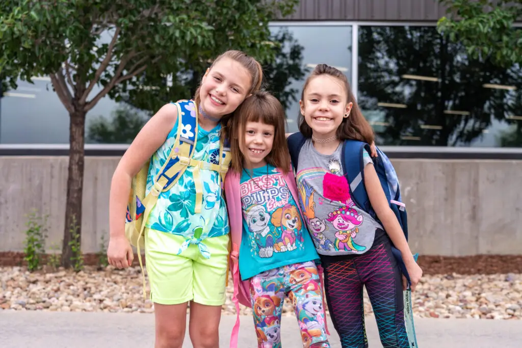 Three sisters smiling together with their new backpacks.