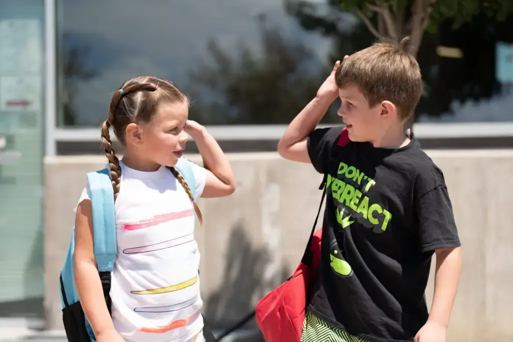 A brother and sister with new backpacks giving each other a high-five.