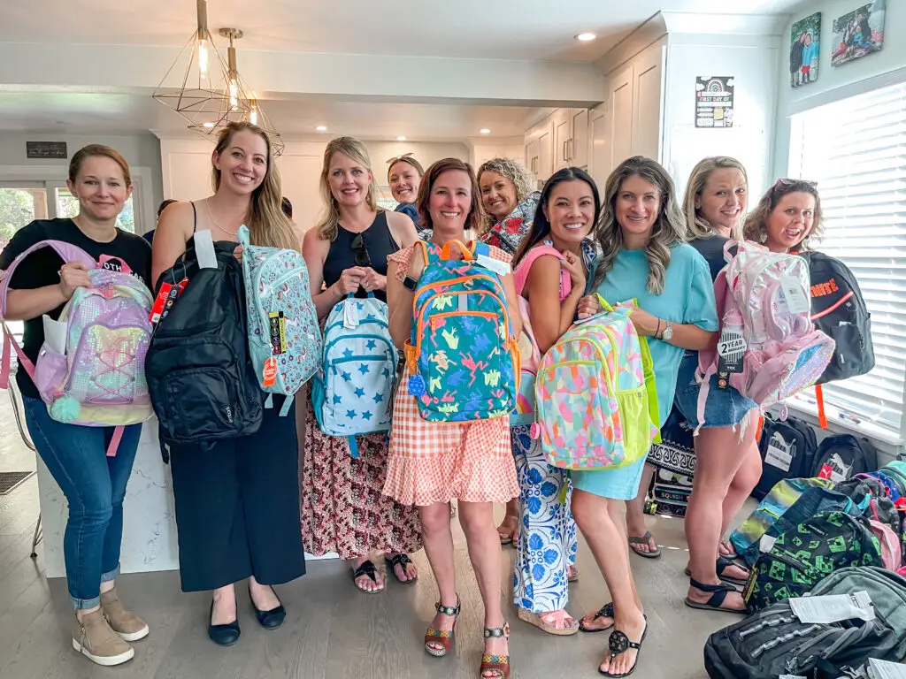 A group of women smiling and showing the many backpacks they filled and prepped together.