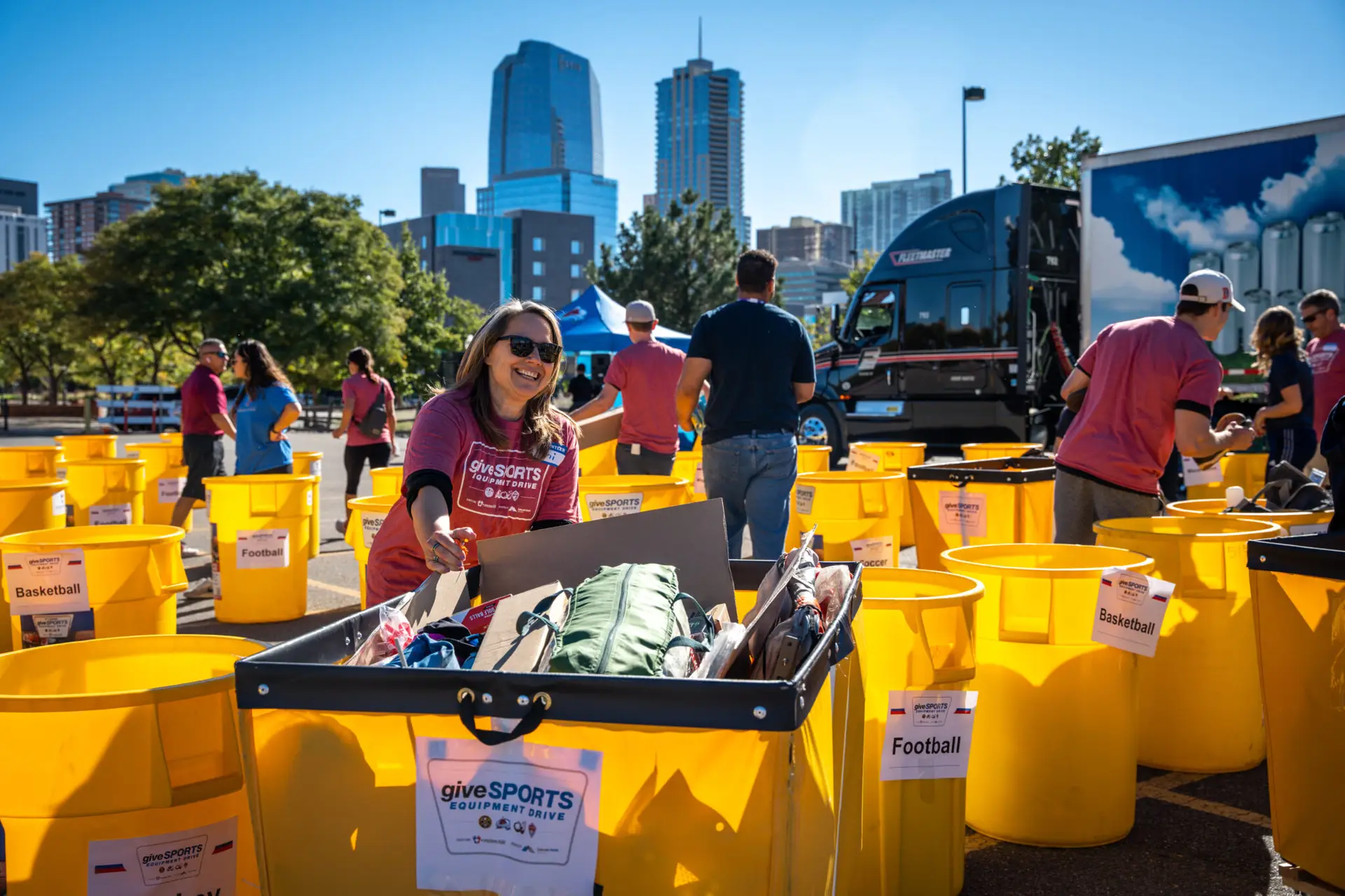 A volunteer smiling with a full donation bin during the giveSPORTS equipment drive.