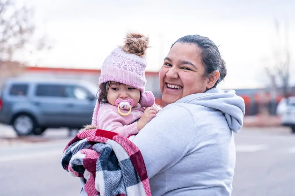 A mother smiling with her baby wrapped in a cozy blanket.
