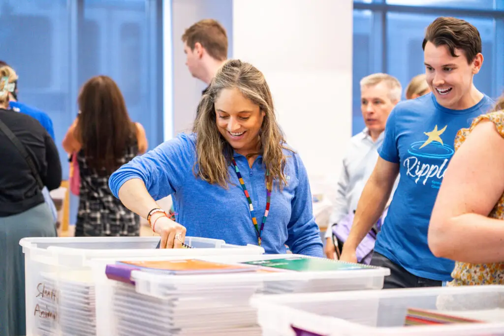 A company working together, smiling, and filling up backpacks with new school supplies.